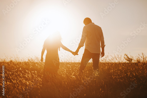 silhouettes of a couple holding hands looking at the bright sunset in a wheat field. photo