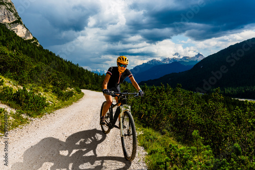 Woman cycling on electric bike on mountain trail. Woman riding on bike in Dolomites mountains landscape. Cycling e-mtb enduro trail track. Outdoor sport activity.