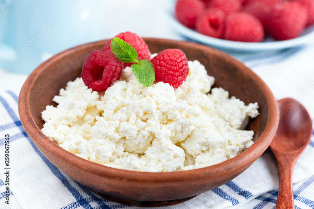 Tvorog or cottage cheese or curd cheese in bowl topped with fresh raspberries and mint leaf. Closeup view