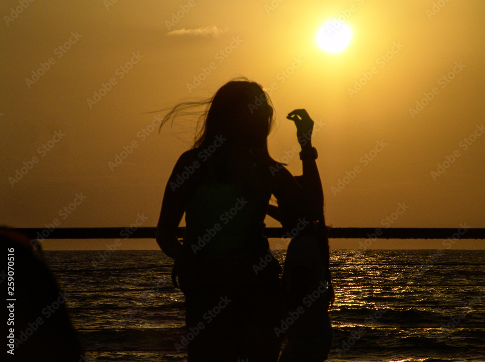 Young woman silhouette posing against the sun on Tel Aviv port boardwalk in front of the Mediterranean sea at sunset