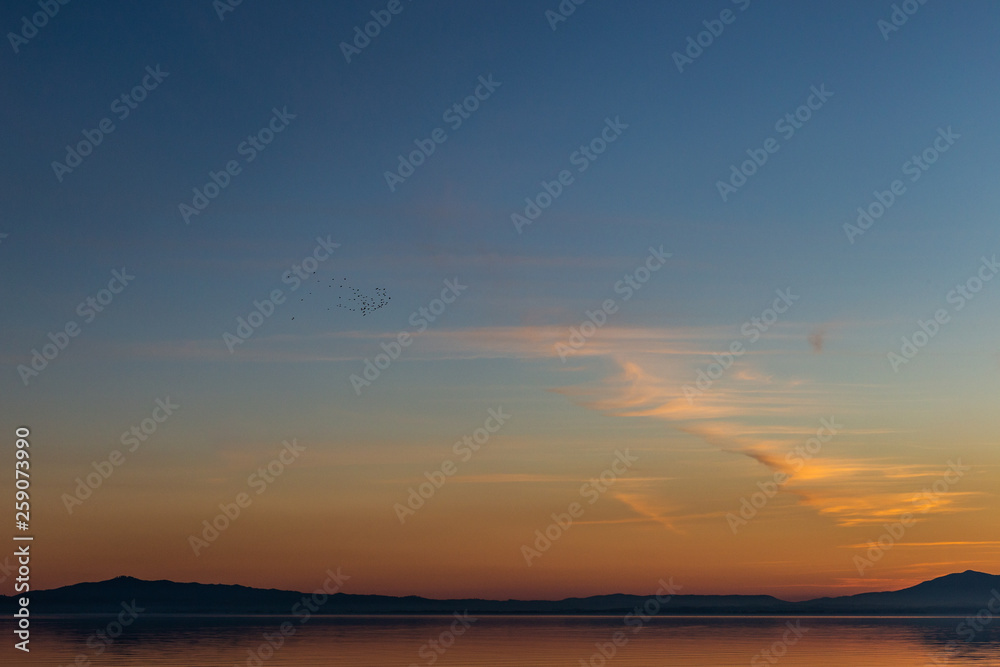 Beautiful view of Trasimeno lake (Umbria, Italy) at sunset, with orange and blue tones in the sky