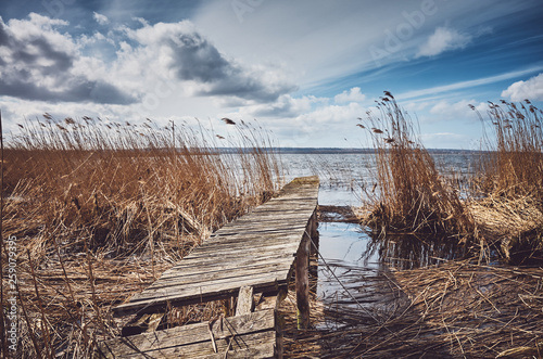 Retro toned picture of an old wooden ramshackle fishing pier in the reeds, selective focus. photo