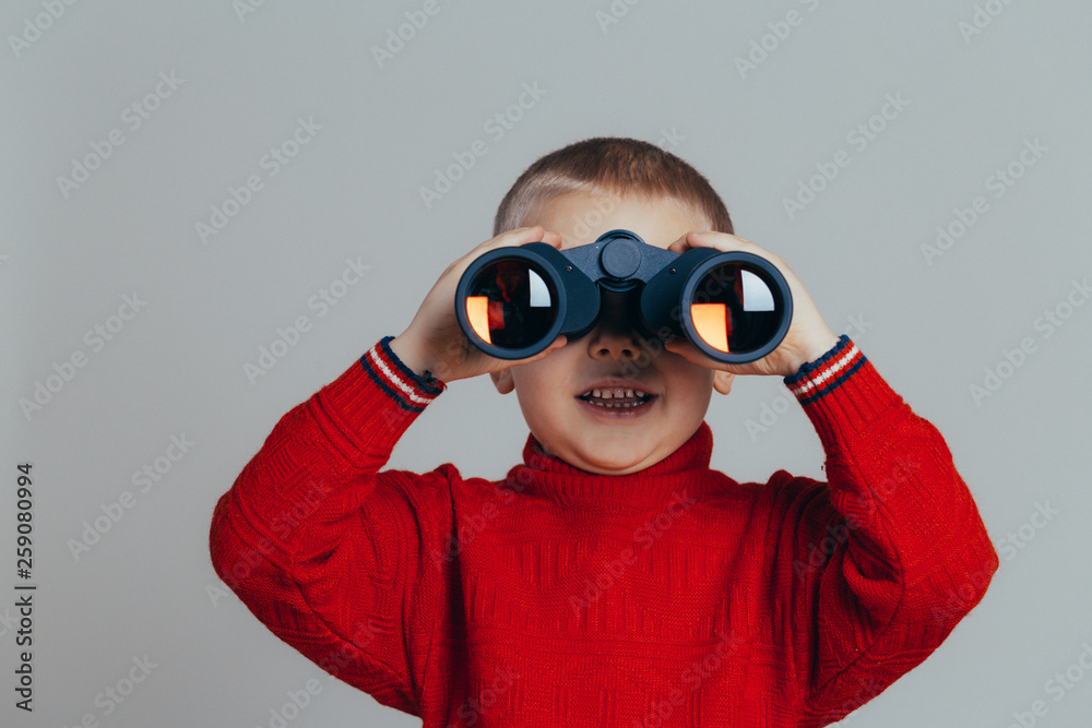 Portrait of attractive smiling boy in red sweater looking through black binoculars close-up Portrait of attractive smiling boy in red sweater looking through black binoculars close-up