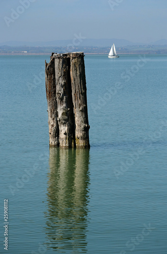 Scenic view of italian Trasimeno Lake with mooring poles on the foreground and sailing boat 