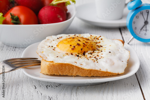 delicious breakfast - hot french toasts, melted emmental cheese and fried sunny side up egg served on a white plate with cup of coffee on a table