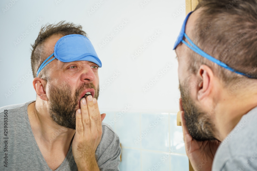 Fototapeta premium Sleepy man looking at mirror and yawning