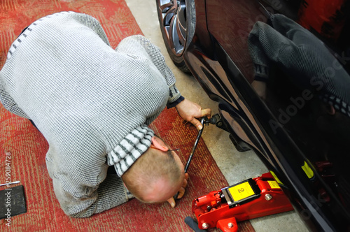 Auto mechanic looking under the car to install the jack