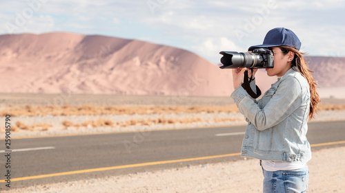 Young Asian woman traveler and photographer holding camera taking photo of sand dune near the road in Namib desert of Namibia, Africa. Travel photography concept © zephyr_p