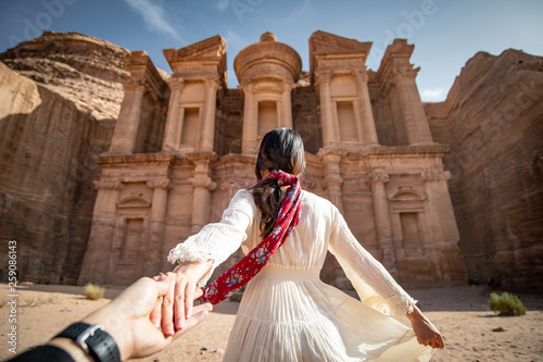 Asian woman tourist in white dress holding her couple hand at Ad Deir or El Deir, the monument carved out of rock in the ancient city of Petra, Jordan. Travel UNESCO World Heritage Site in Middle East photo
