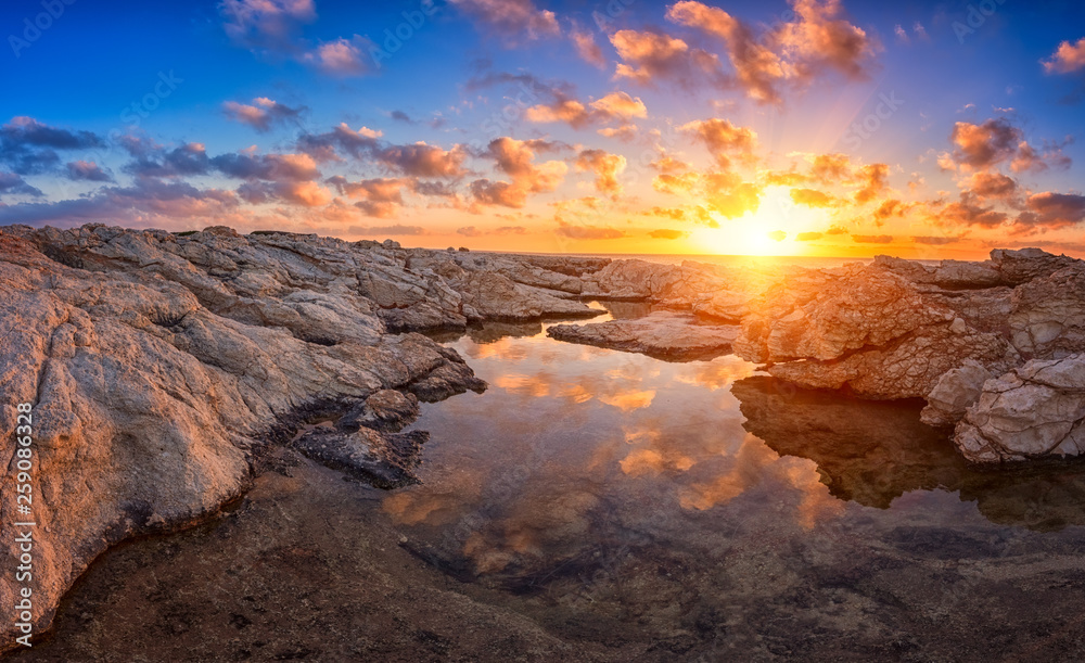 Amazing sunset on the white rocks with sun, blue sky, clouds and reflection in the water, Cyprus. Outdoor travel background, panorama
