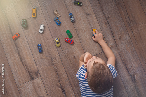 Child playing with miniature toy cars on wooden floor. Top view