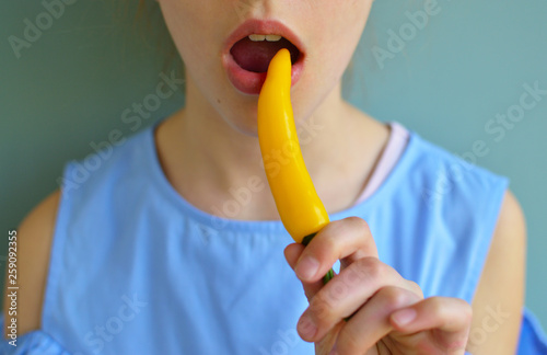 Crop shot of girl eating yellow chili pepper