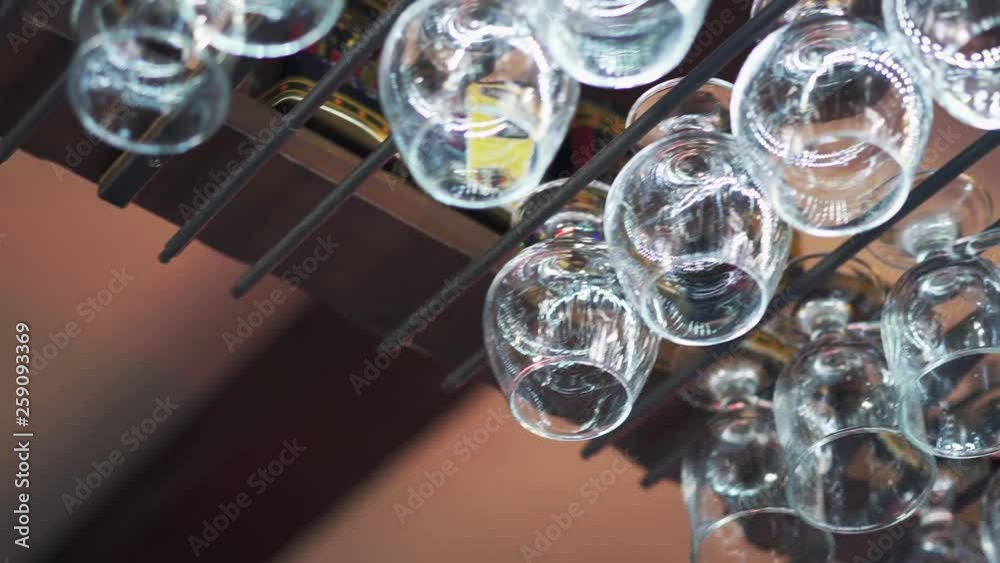 Empty clean wine glasses hanging above a bar rack. Man's hand takes one crystal glass from a metal rack. Close-up Empty clean wine glasses hanging above a bar rack. Man's hand takes one crystal glass from a metal rack. Close-up