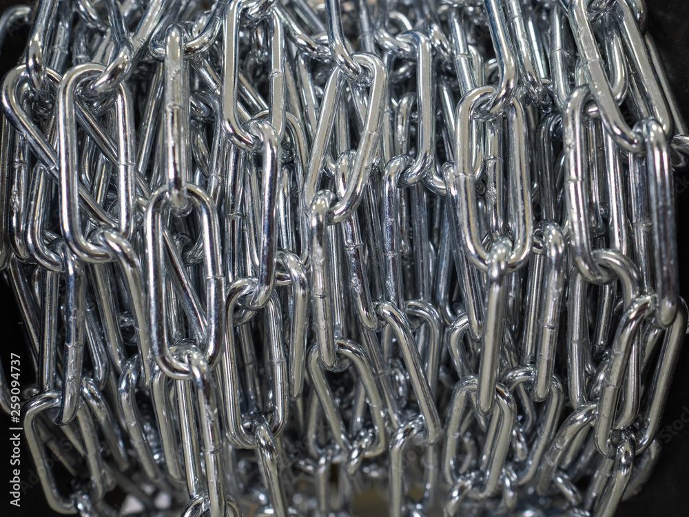 The steel chain is reeled up on the coil in shop. The brilliant chain twisted in a roll. Long industrial chain The steel chain is reeled up on the coil in shop. The brilliant chain twisted in a roll. Long industrial chain