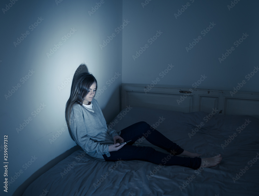 Depressed teenager girl on mobile phone victim of cyberbullying feeling sad, unhappy and lonely