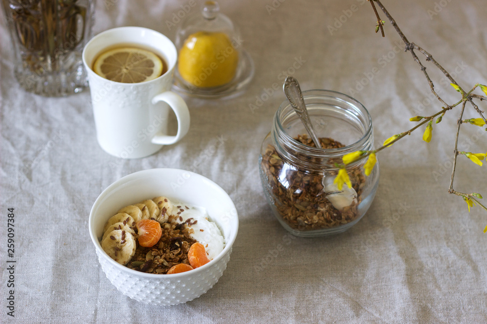 Breakfast of granola with yogurt and tea and forsythia flowers on a linen tablecloth. Rustic style. Breakfast of granola with yogurt and tea and forsythia flowers on a linen tablecloth. Rustic style.