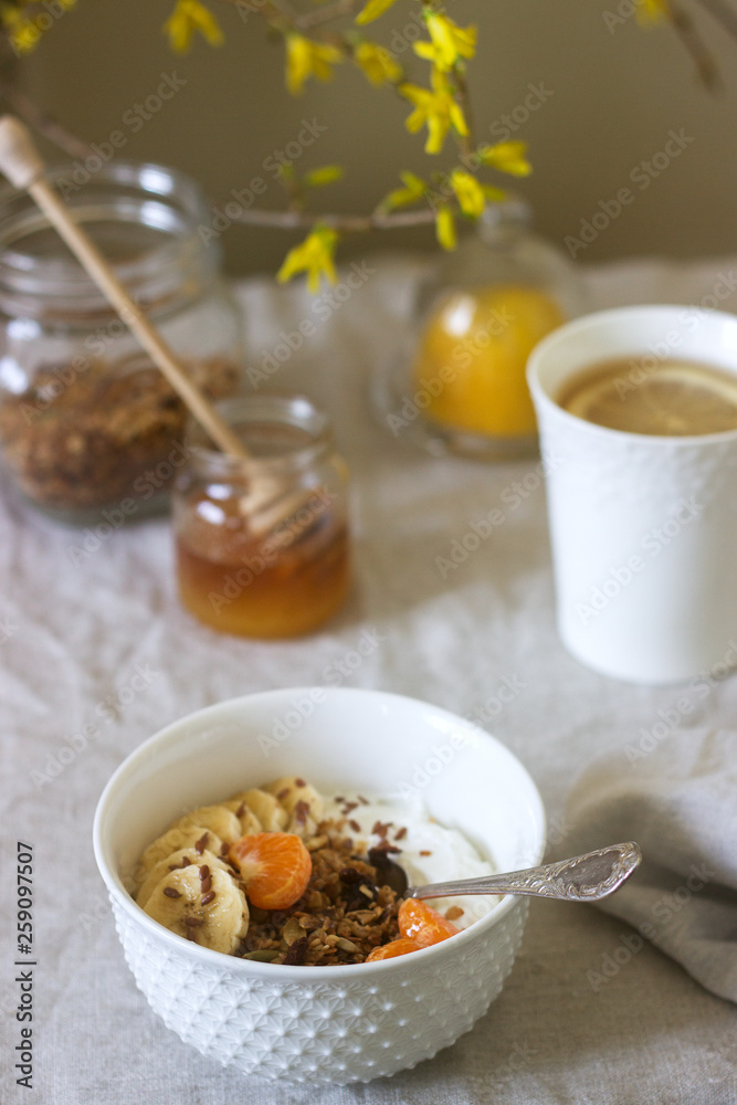 Breakfast of granola with yogurt and tea and forsythia flowers on a linen tablecloth. Rustic style.