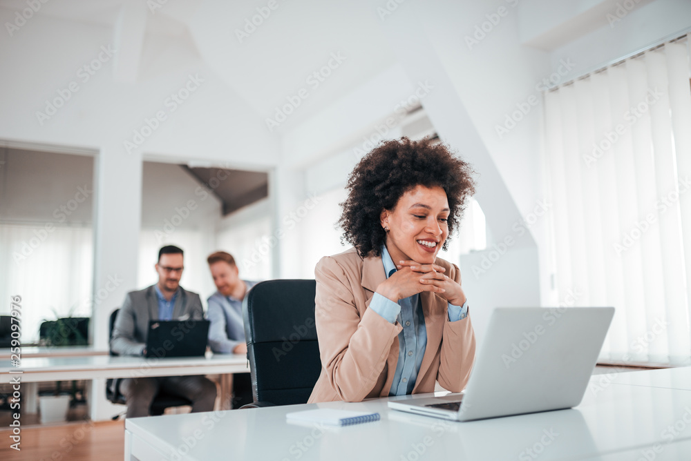 Beautiful mixed-race businesswoman looking at laptop in co working office.
