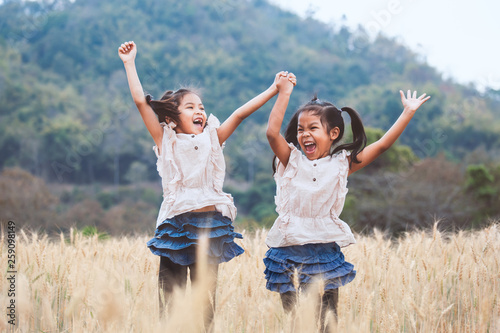 Two happy asian child girls having fun to play and jump together in the barley field