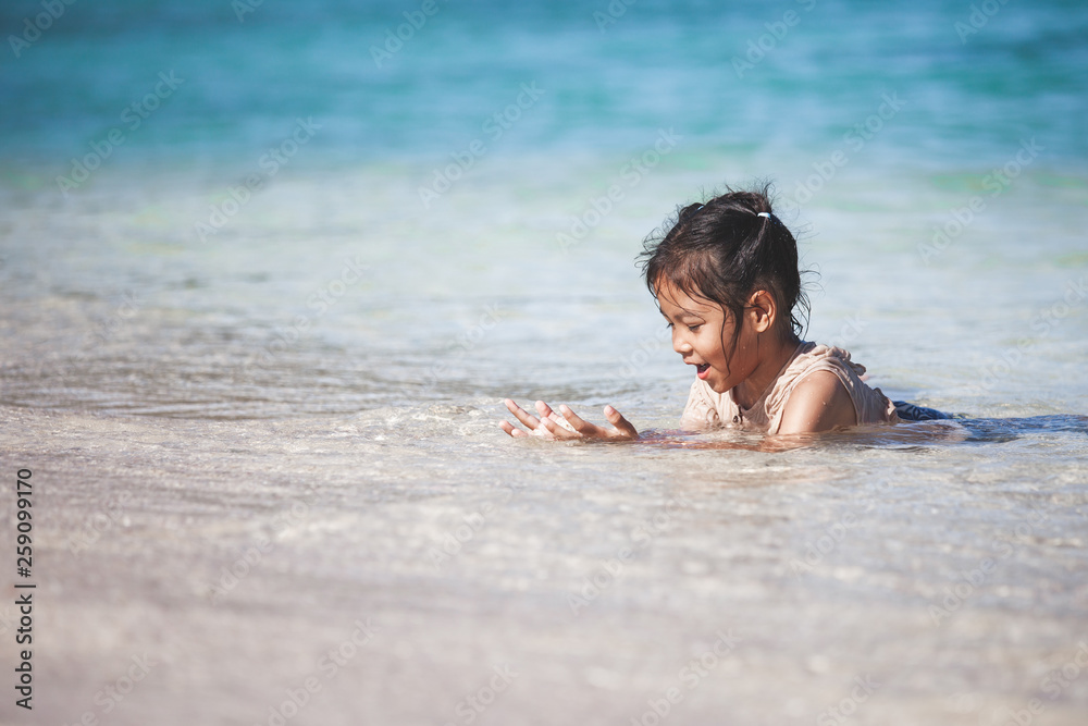 Happy asian child girl having fun to play water in the beautiful sea in summer vacation