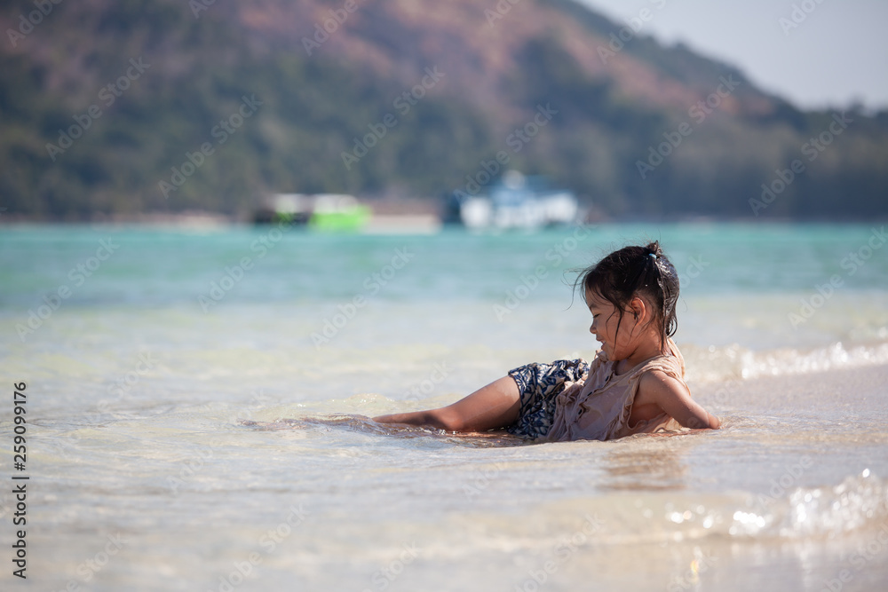 Happy asian child girl having fun to play water in the beautiful sea in summer vacation