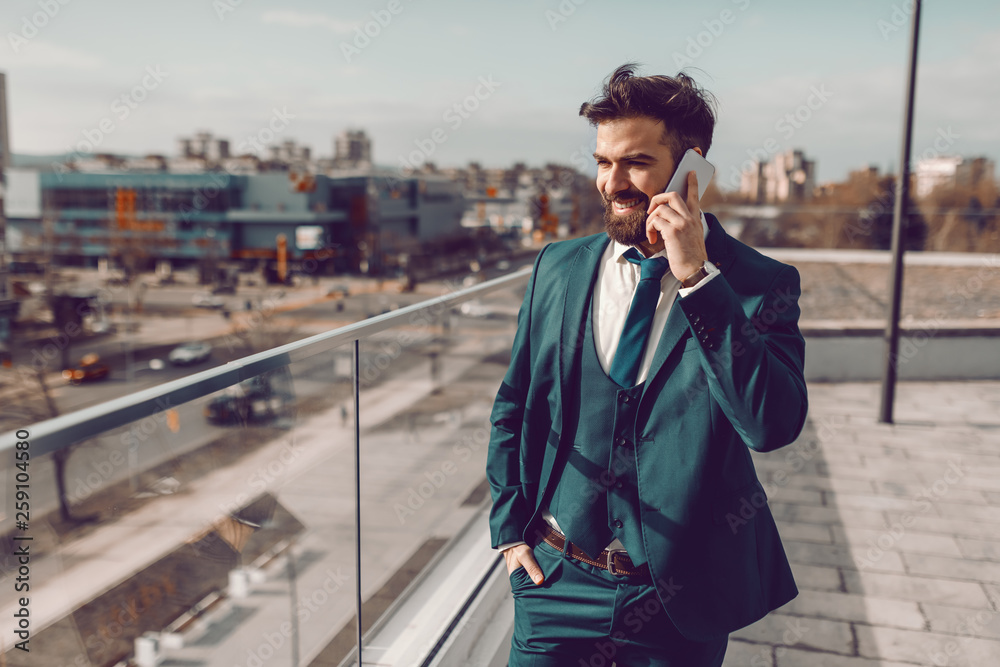 Young perspective bearded Caucasian businessman in formal wear using smart phone for business talk while standing on rooftop. Great things never came from comfort zones. Young perspective bearded Caucasian businessman in formal wear using smart phone for business talk while standing on rooftop. Great things never came from comfort zones.