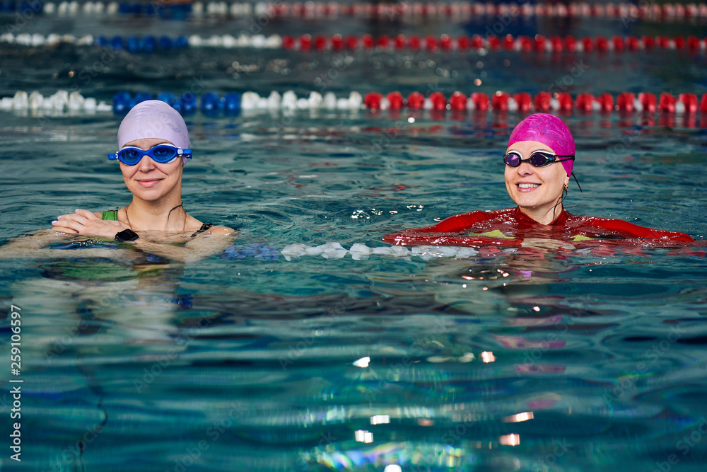 Two smiling swimmer women relaxing in the pool after a swim.