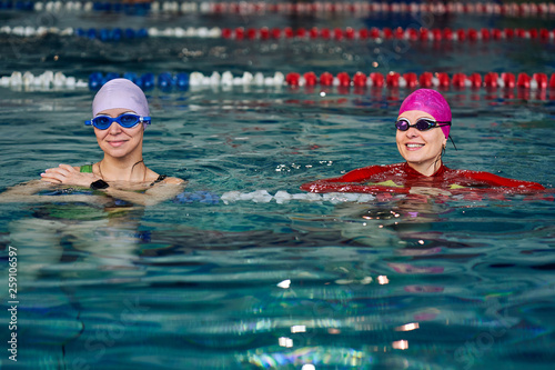 Two smiling swimmer women relaxing in the pool after a swim.