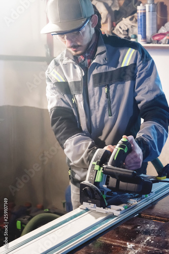 Portrait of a young carpenter joiner with manual circular power saw in the hands of a worker in a home workshop. Starting a business. Craftsman