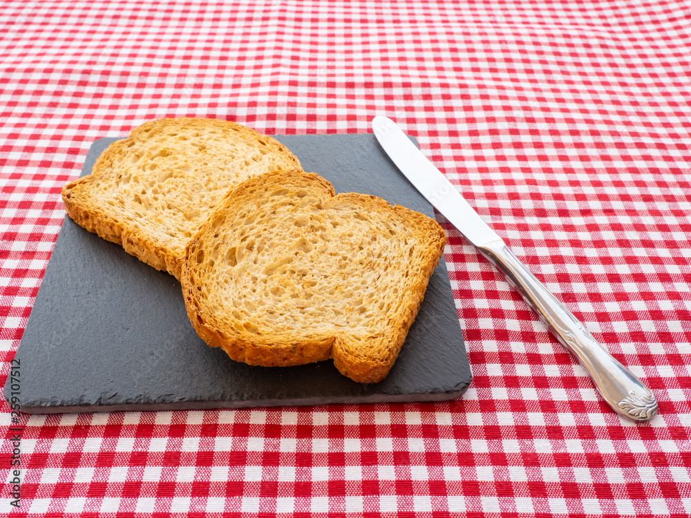 Two slices of toast on a slate plate, one knife and tablecloth vintage style Two slices of toast on a slate plate, one knife and tablecloth vintage style