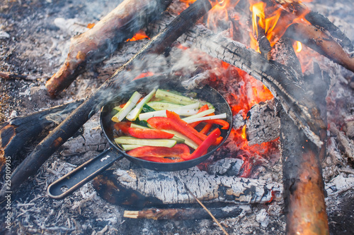 Cooking dishes from red bell peppers and cucumbers in a pan on a fire