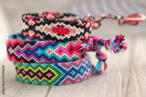 Three colorful handmade homemade natural woven bracelets of friendship on wooden background, rainbow colors, checkered pattern