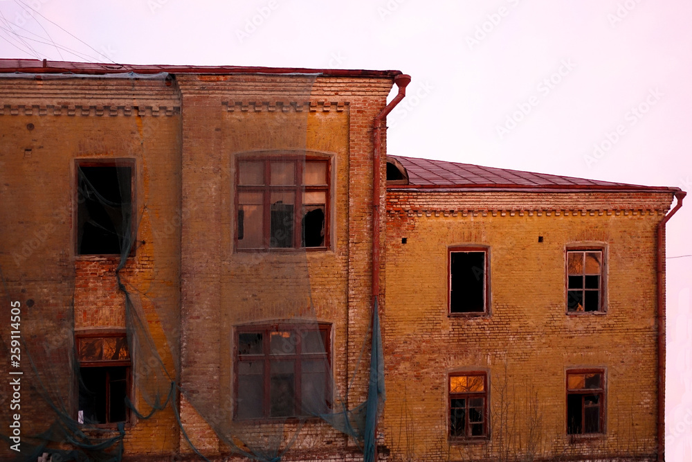 Empty destroyed building with broken windows. Pink sky Sunset. Photo in red colors. The oppressive atmosphere of destruction. Scenery for a horror movie