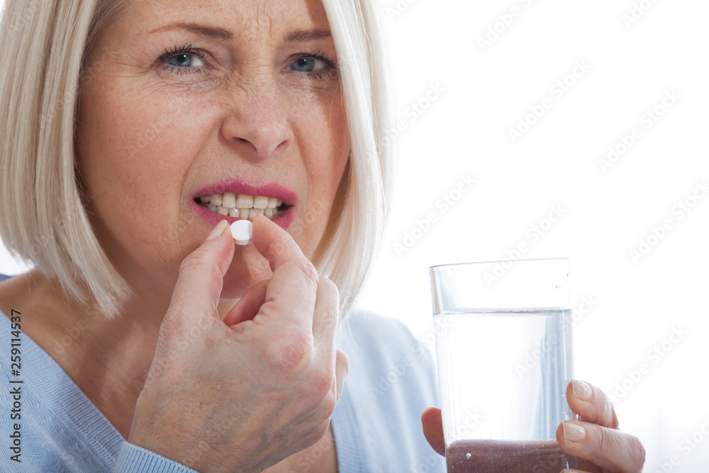 Sick frustrated woman feel unwell holding glass of water and pill doubting to take medicine, exhausted female suffer from migraine or headache ready to have antibiotic or painkiller to ease symptoms