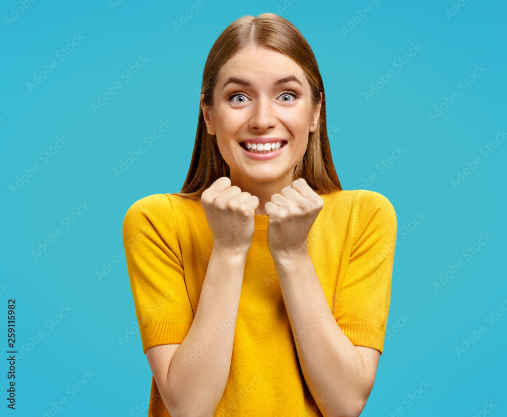 Φωτογραφία Young girl stares at camera with eyes full of happiness, holds hands clenched in fists