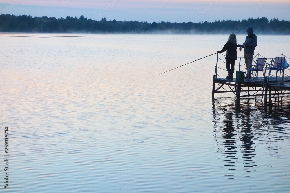 angler with a girl fishing at a lake at sunset