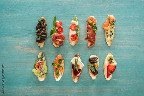 top view of italian bruschetta with salmon, dried tomatoes, prosciutto and herbs on wooden table