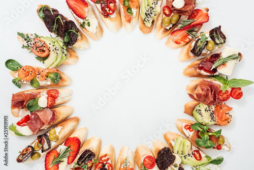 top view of round frame made of delicious italian bruschetta with salmon, prosciutto, herbs and various fruits with vegetables