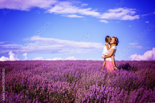 Happy little sisters with their mother are in a lavender field holding bouquet of purple flowers
