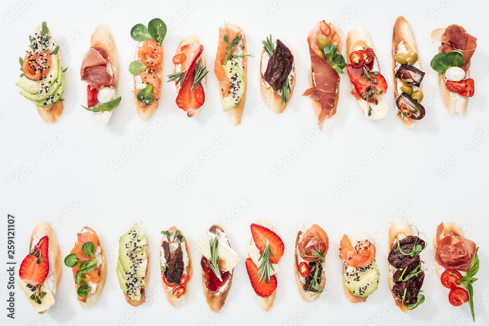 top view of traditional italian bruschetta with prosciutto, salmon, fruits, vegetables and herbs on white with copy space