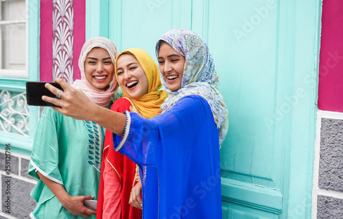 Canvas Print Happy arabian friends using smartphone for making selfie story on social network