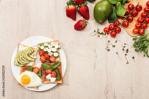 top view of delicious toasts with vegetables on plate and fresh ingredients on wooden table