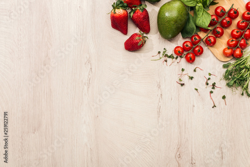 top view of strawberries, cherry tomatoes, avocado and basil on wooden table with copy space