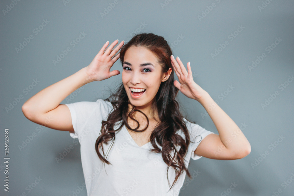 Funny portrait of happy asian young woman with dark long hair in white t-shirt on grey background Funny portrait of happy asian young woman with dark long hair in white t-shirt on grey background