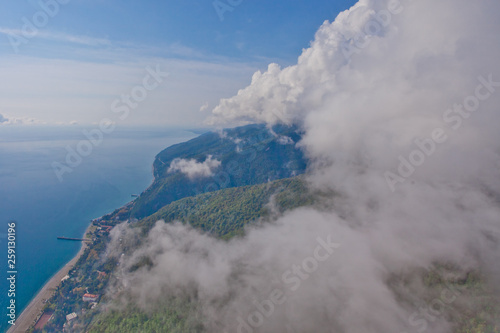 Flying over the bright beautiful green shore and over the blue sea next to the white fluffy clouds. Aerial photo from  in the Caucasus in Abkhazia © Mikhail Semenov