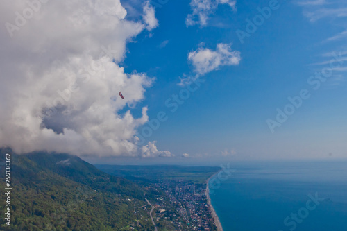 Flying over the bright beautiful green shore and over the blue sea next to the white fluffy clouds. Aerial photo from  in the Caucasus in Abkhazia