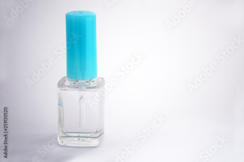 Closed bottle of clear nail polish for manicure on a light background. Clear transparent nail polish bottle with blue screw cap. Clear nail polish with copy space, moke up. Manicure concept.
