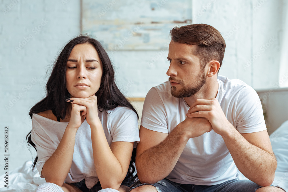 Φωτογραφία handsome man in jeans and beautiful woman in t-shirt sitting on bed in bedroom