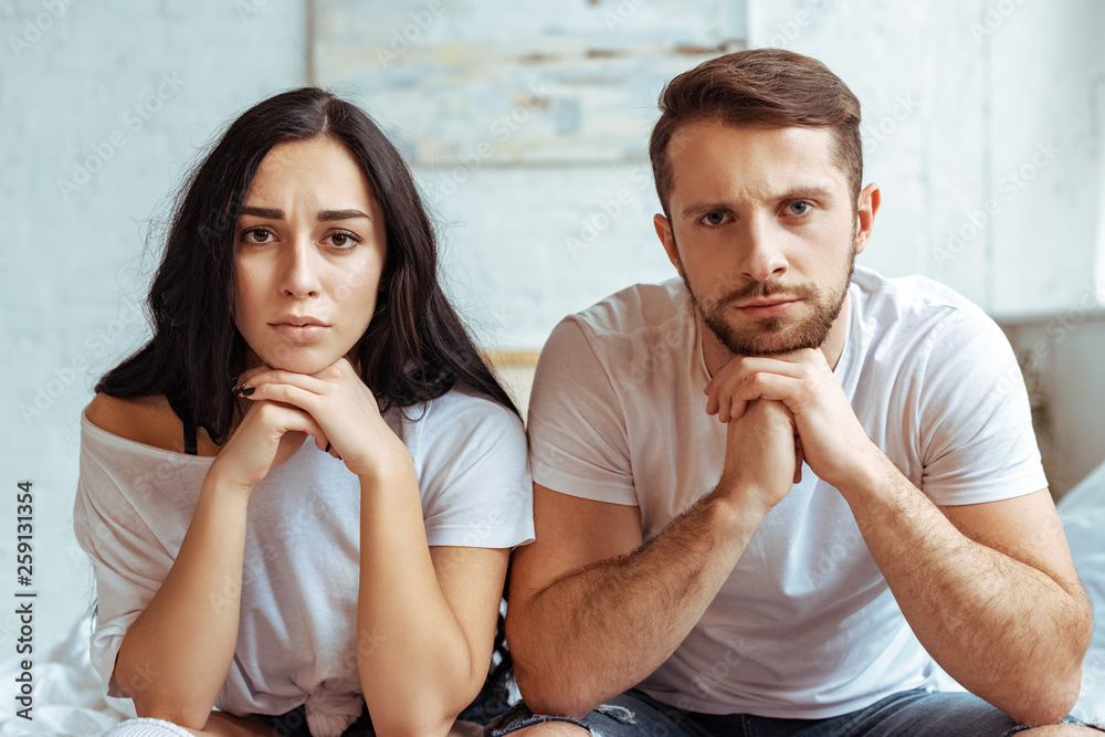 Φωτογραφία handsome man in jeans and beautiful sad woman in t-shirt sitting on bed and look