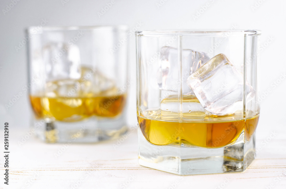 Two glasses of scotch whiskey with ice cubes, white background, wooden backdrop Two glasses of scotch whiskey with ice cubes, white background, wooden backdrop